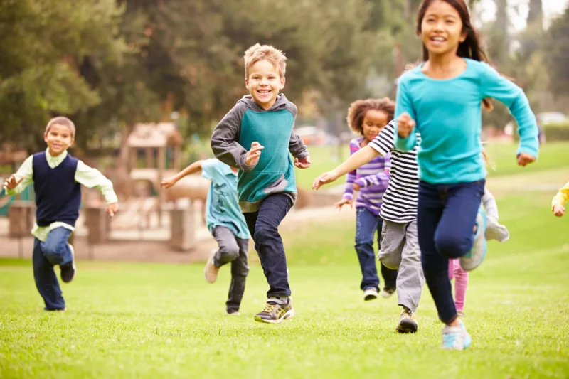 Group of young children running in park with playground in background