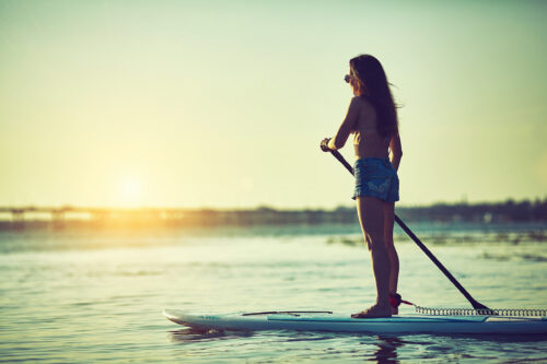 woman on stand up surf board with paddle at sunset on lake