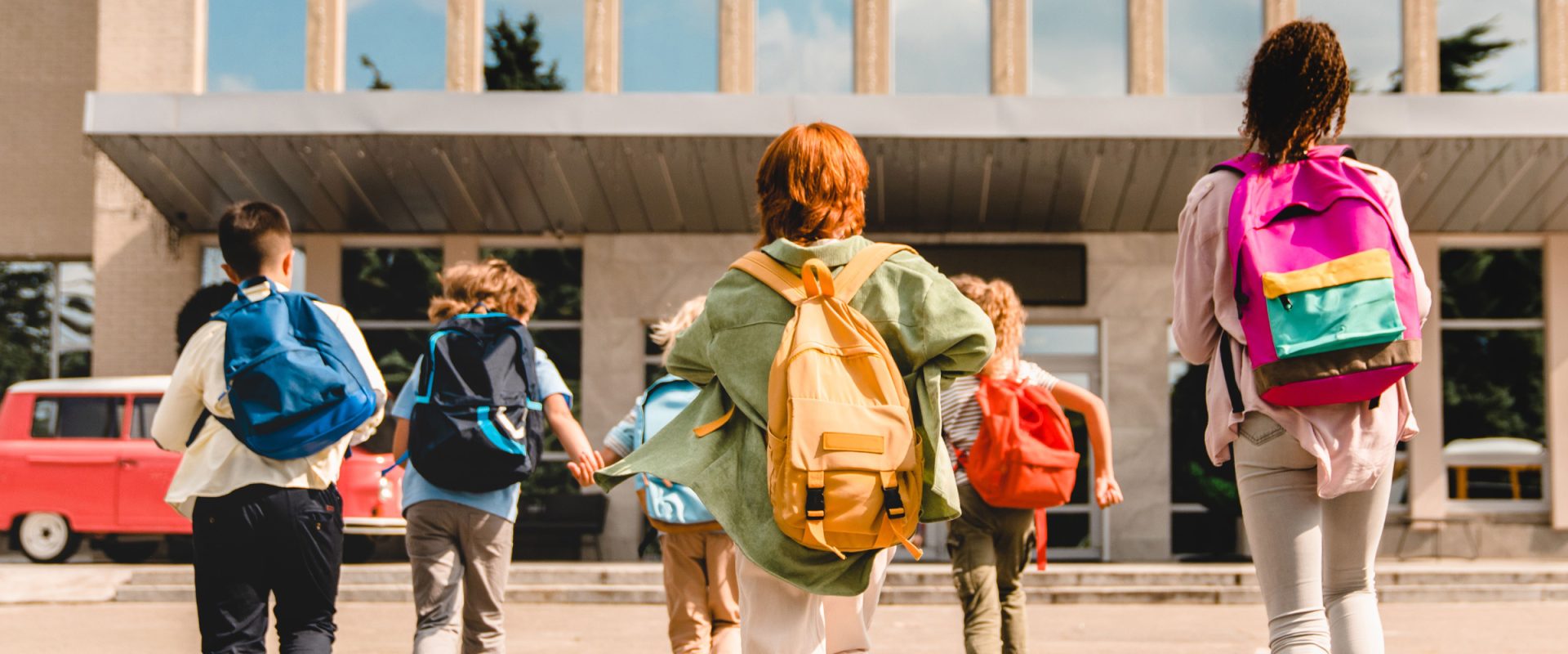 group of children wearing backpacks running into school