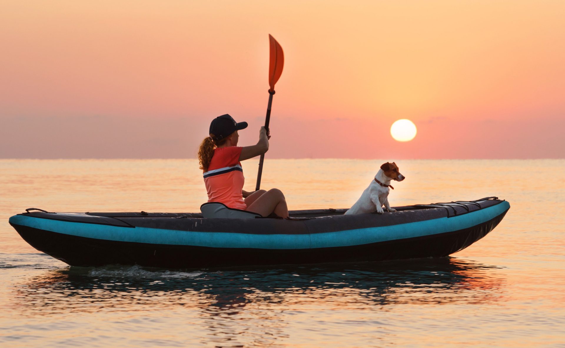 woman rowing an inflatable kayak with dog Jack Russell Terrier at sunrise
